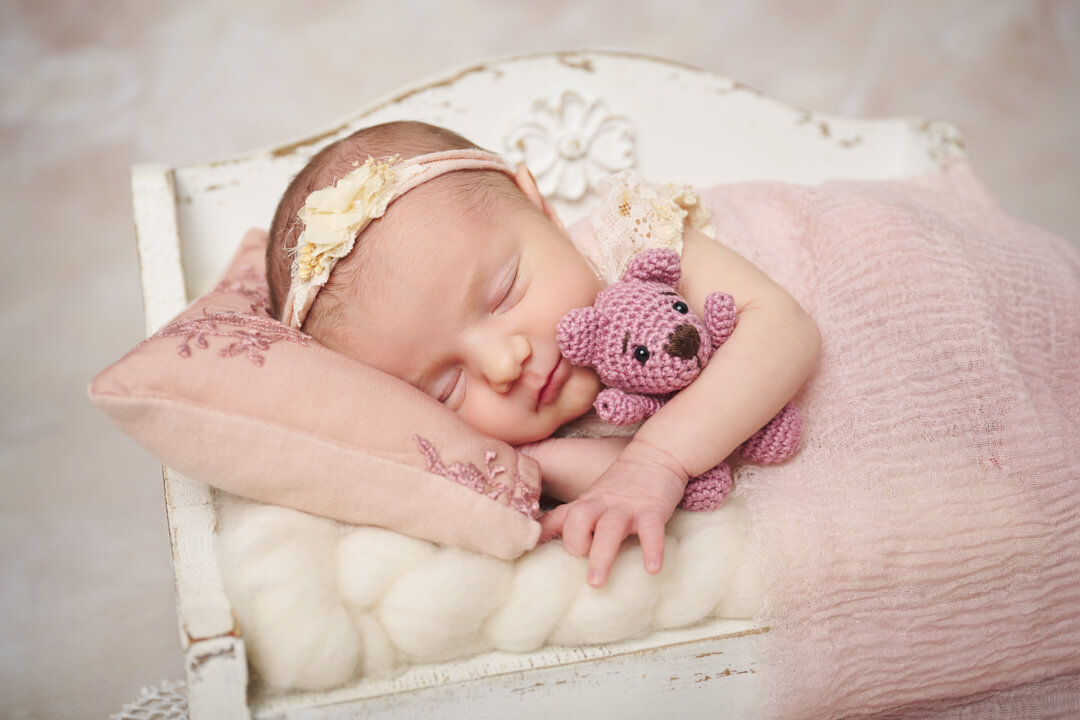 Neugeborenenfotoshooting, Baby in Seitenlage auf Holzsofa mit Häkeltier im Arm Babyfotografie Ingolstadt Mandy Limbach Fotografie