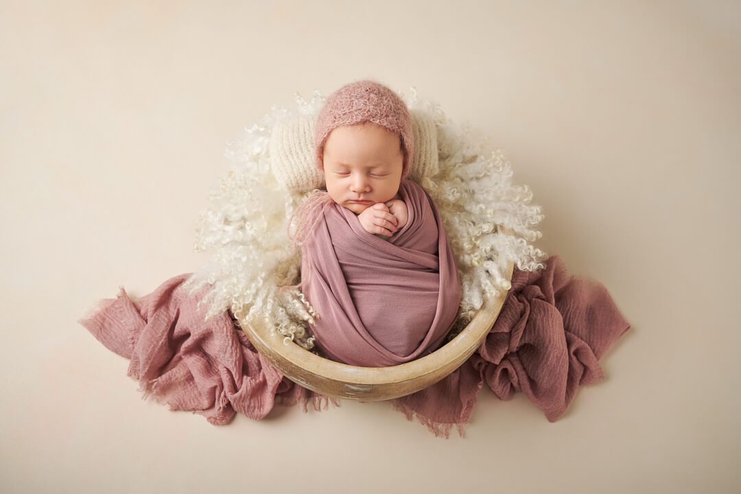 Neugeborenes mit Mütze liegt in ein Tuch gewickelt in einer Holzschale bei Mandy Limbach Fotografie