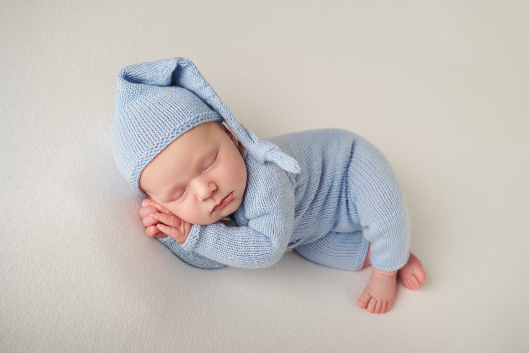 Neugeborenes liegt seitlich schlafend auf schlichter Decke im süßen Outfit, Studio Neugeborenenfotografie