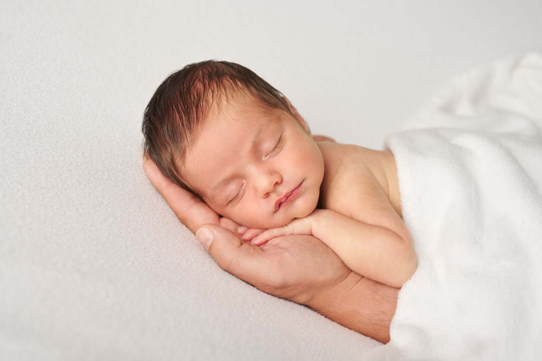 Neugeborenes liegt mit Köpfchen auf Papas Hand auf schlichter Decke, halb zugedeckt, Studio Neugeborenenfotografie Vohburg
