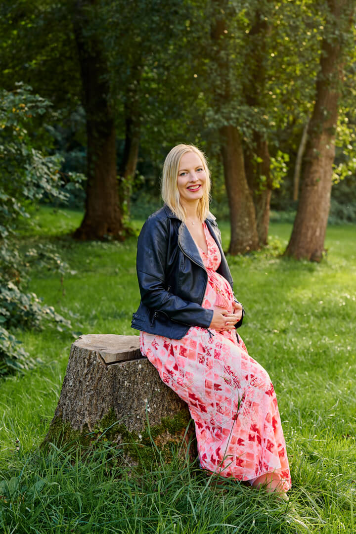 Babybauchfotografie, schwangere Frau in gemustertem Kleid in Natur, sitzend auf Baumstamm, Mandy Limbach Fotografie